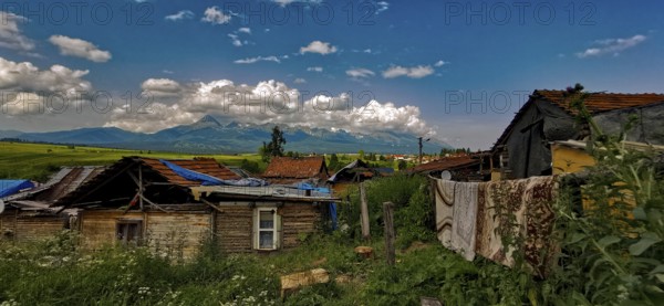 Rural scene with huts and mountains under a wide cloudy sky, atmospheric atmosphere, bright colors, Roma settlement, Slovakia