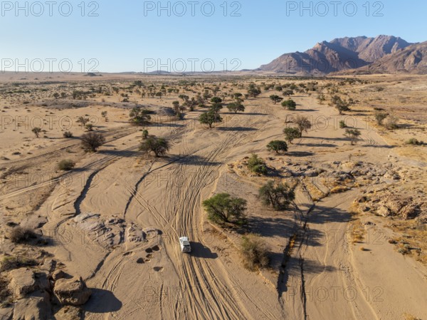 Aerial view of off-road car driving in dry riverbed and desert landscape on the Ugab River, behind Brandberg, Erongo, Damaraland, Namibia