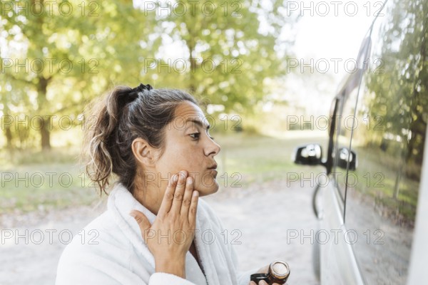 A woman enjoys her skincare routine while experiencing the freedom of van life in autumn. Captured in New Zealand, the serene moment highlights her connection to nature