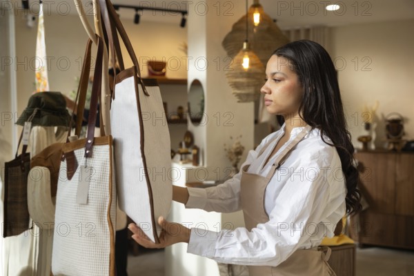 A woman carefully examines a large handbag displayed in a stylish, well lit bag store. The setting features cozy lighting, earthy tones, and a range of accessories for sale