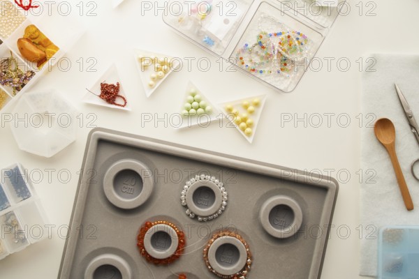 Top view of a creative jewelry making setup in a studio with tools like scissors, a wooden spoon, bead sorting trays, and a bracelet mandrel highlighting handmade craftsmanship