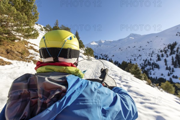 A man rides a snowmobile through a pristine winter landscape, surrounded by snow-capped mountains and evergreen trees under a clear blue sky, capturing the thrill of winter adventure