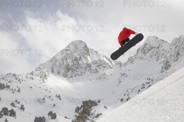 A snowboarder in vibrant gear catches air while performing a jump against a backdrop of majestic snow-capped mountains, embodying the thrill of winter freeride adventure