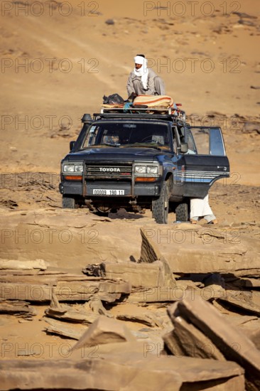 An off-road vehicle with people in traditional clothing stands in a vast desert landscape, Off-road vehicle through the Sahara desert in Algeria