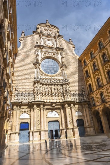 The imposing facade of the montserrat monastery, featuring intricate details and a large rose window, basks in the sunlight, casting shadows across the courtyard
