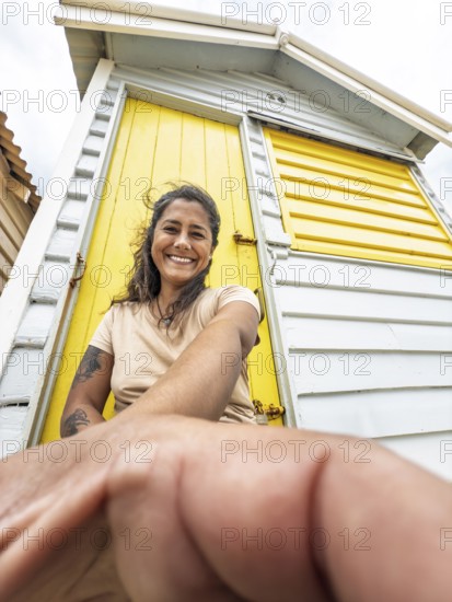 A woman smiles while leaning against a brightly painted yellow Brighton Bathing Box in Melbourne, Australia. The iconic beach sheds are a popular tourist attraction