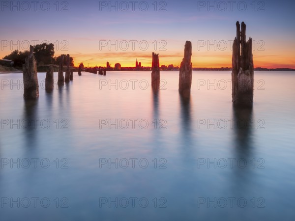 View at sunset over the Strelasund of the skyline of the city of Stralsund with its churches and warehouses in the harbor, in front of old groves, Stralsund, Mecklenburg-Western Pomerania, Germany