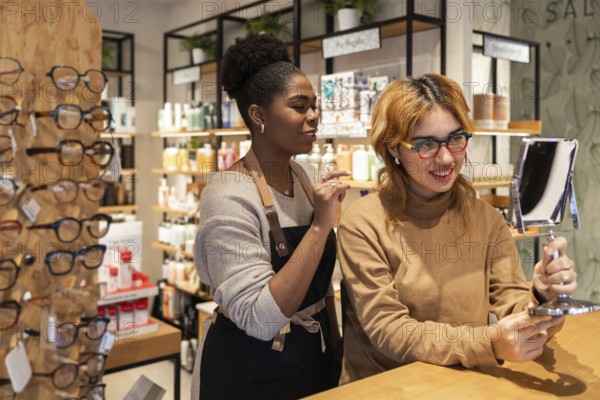 Two women in a cosmetics store engage in a friendly interaction. One is holding a mirror, while the other provides assistance. Shelves filled with beauty products surround them