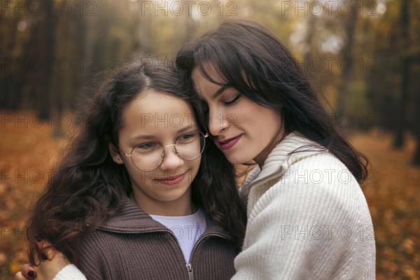 A touching moment of a mother and daughter embracing in an autumn forest. Surrounded by warm, golden leaves, they share a comforting and loving connection during fall