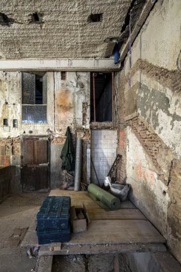 A partially renovated space shows exposed brick, peeling plaster, and construction materials scattered across the site. The aged walls and wooden door highlight the restoration process in progress