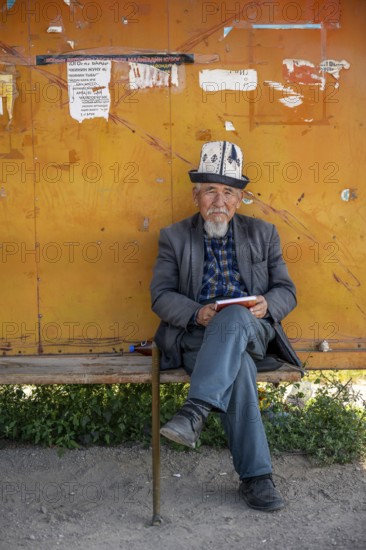 Local man with traditional hat waiting at a bus stop, Issyk-Kul region, Kyrgyzstan