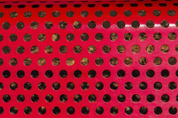 Close-up of vibrant red painted metal sitting bench backrest with perforated round holes, Quebec, Canada