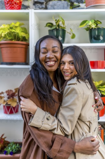 Two multi ethnic female friends are hugging each other with eyes closed in a plant shop, celebrating their friendship and enjoying a relaxing moment together
