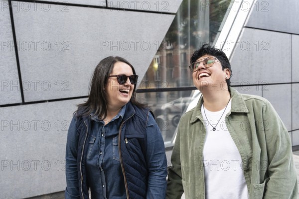 A happy lesbian couple enjoying a sunny day, laughing together outdoors in an urban setting. They radiate joy and connection, celebrating diversity and love