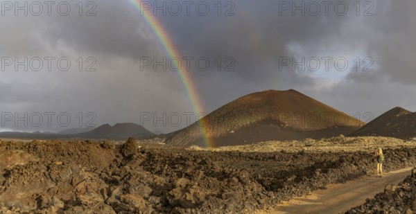 A vibrant rainbow arcs over the rugged volcanic terrain of Timanfaya National Park in Lanzarote, Canary Islands, creating a striking contrast against the stormy sky