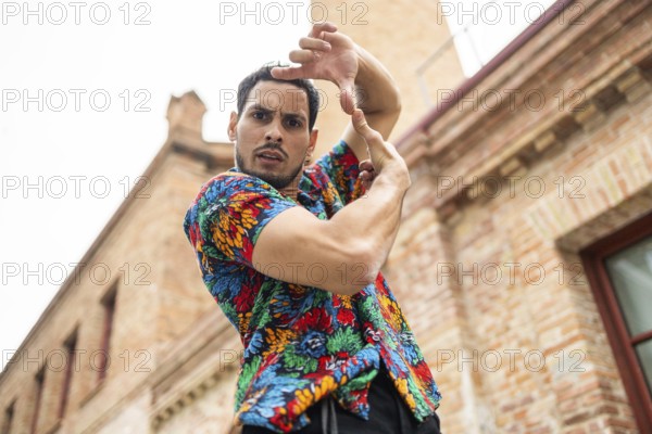 A male dancer in a vibrant, patterned shirt strikes a dynamic pose against a brick building background. The image captures the energy and passion of Cuban dance