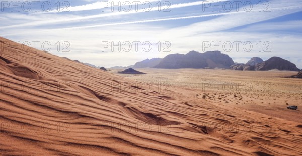 Captivating view over the red sand dunes in Wadi Rum Desert, Jordan, under a clear sky, with distant mountains and a lone vehicle visible