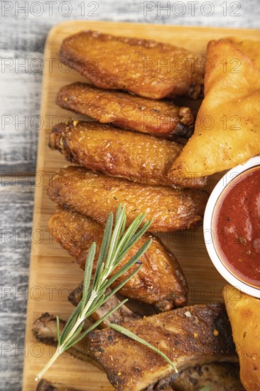 Set of snacks: nachos, chicken wings, fried ribs, bean tortillas on a cutting board on a gray wooden background. Top view, flat lay, close up