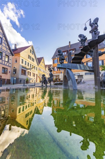 Reflection of traditional houses in a decorative water basin with sculptures under a blue sky, Weil der Stadt, Böblingen district, Germany