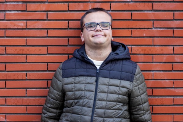 Man with an intellectual disability smiles warmly while leaning against a brick wall. His relaxed posture and stylish winter jacket highlight confidence, inclusion, and positivity in an urban setting