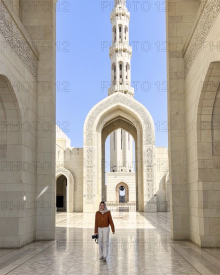 A woman wearing an headscarf walks through the grand architecture of the Sultan Qaboos Mosque in Muscat, Oman, showcasing its intricate designs