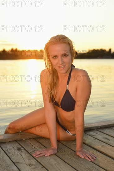 Woman in a bikini sitting on a dock by the water at sunset, Austria