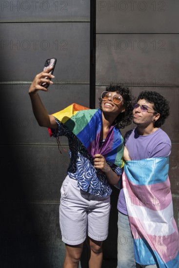 A joyful multiethnic LGBTQ+ couple takes a selfie wrapped in pride flags, celebrating love, diversity, and inclusivity in a vibrant and uplifting moment