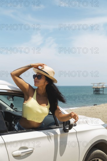 A young Latin woman in a yellow top and sunglasses enjoying the breeze and ocean view from a car at the popular Mancora beach, Peru. Perfect summer vibe