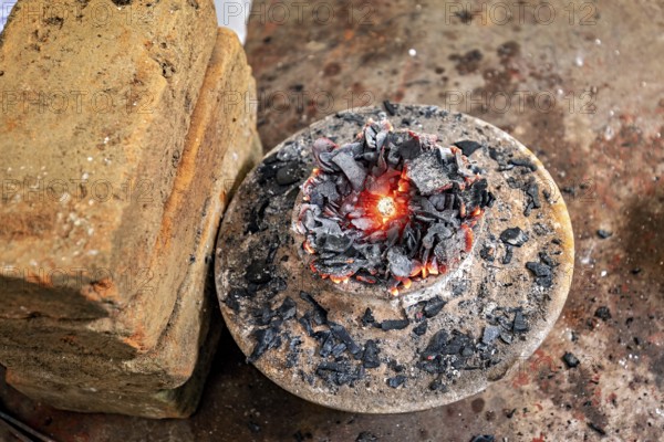 Close-up of a fire pit with embers and coals on metal plate with bricks piled next to it, a kiln for sapphires in the city of Ratnapura in Sri Lanka
