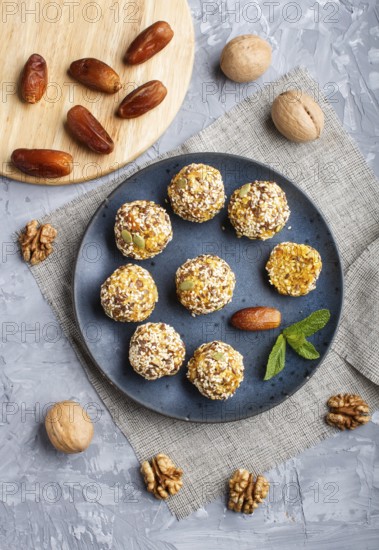 Energy ball cakes with dried apricots, sesame, linen, walnuts and dates with green mint leaves on a blue ceramic plate on a gray concrete background. linen napkin, top view, close up, flat lay. vegan homemade candy