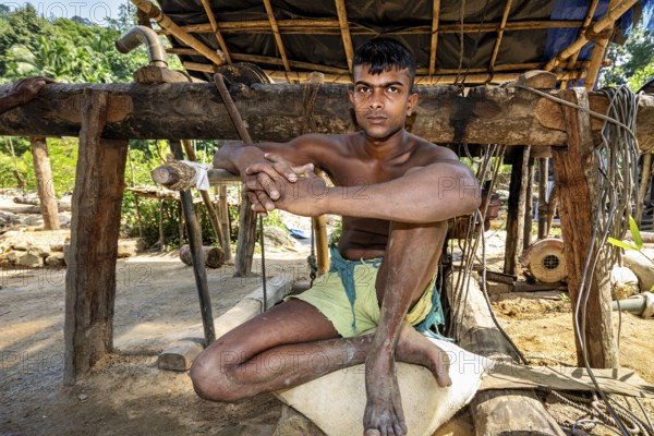 A young man sits relaxed in a rustic outdoor wooden structure, the sapphire and gemstone mines at Ratnapura in Sri Lanka