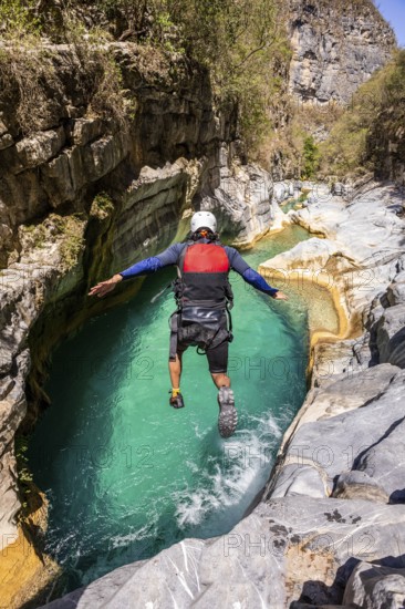 A canyoneer leaps into vibrant turquoise waters surrounded by rugged cliffs in Matacanes, Nuevo Leon, Mexico, enjoying a thrilling day of canyoning and exploration