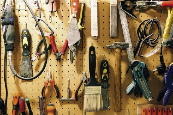 Pegboard displaying assorted luthier tools for crafting bass guitars, including pliers, brushes, files, and more, organized neatly, reflecting craftsmanship and precision