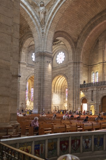 Interior view of a church with high walls and visitors in rows of seats, Paris
