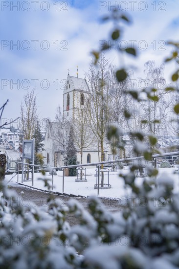 Snow-covered church with decorated tower behind trees and bushes, Aidlingen, Böblingen district, Germany