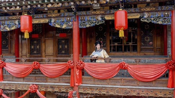 A woman in traditional Qing Dynasty attire stands on a beautifully decorated balcony in Pingyao, China. Red lanterns and intricate woodwork adorn the historical setting