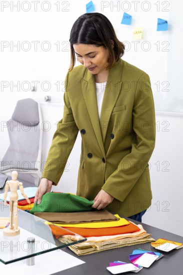 A professional image consultant in an office setting carefully selects vibrant fabrics for a fashion project. A palette of colorful swatches and notes adorns the workspace, enhancing creativity