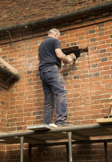 Builder removing red bricks to make window space, Suffolk, England, UK
