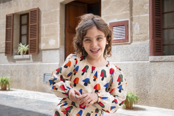 A joyful child, dressed in colorful attire, plays in the sunlit street of a quaint village, expressing happiness and innocence amidst charming rustic surroundings