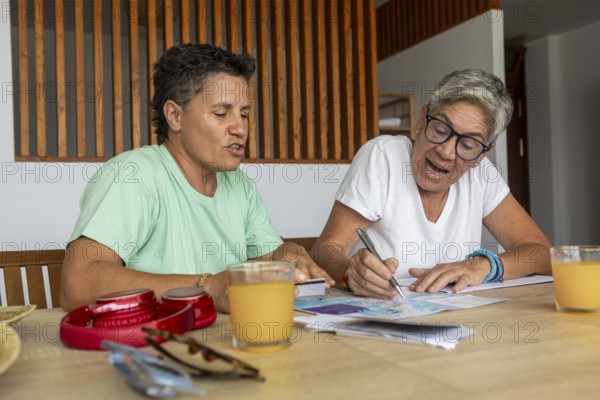A lesbian couple is focused and active as they plan their summer holidays, marking details on travel brochures and discussing options excitedly over breakfast