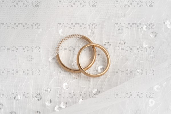 Close-up of two intertwined rose gold wedding rings atop a delicate white lace fabric, symbolizing eternal love and commitment