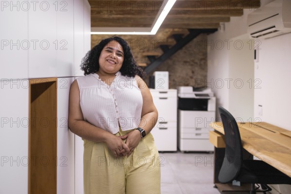 A young woman stands in a modern coworking space with a warm smile. The open office setting is ideal for startups and creative work. She appears relaxed and confident