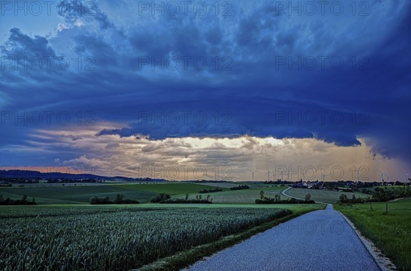 Aufziehendes Gewitter mit imposanter und bedrohlicher Wolkenformation einer Gewitterzelle über einem Dorf mit Windrädern im Hintergrund, Baden-Württemberg, Deutschland