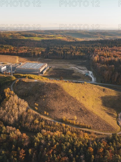 Building complex in an autumnal landscape with colourful forest and rolling hills in the evening light, Lindenrain industrial estate, Gechingen, Black Forest, Germany
