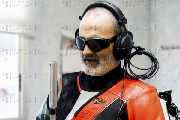 A blind marksman, wearing headphones and protective gear, concentrates during training. The image captures the precision and determination of adaptive sports in shooting