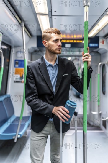 Young businessman commuting on a subway train, holding a reusable coffee cup and luggage, looking thoughtfully ahead