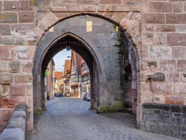 Alley with cobblestones leads through the town gate Oberes Tor, view through the gate to the half-timbered houses of the old town in the evening light, Wolframs-Eschenbach, Middle Franconia, Bavaria, Germany
