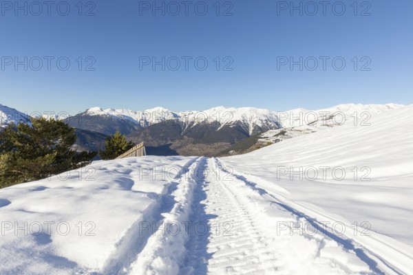 A pristine snowmobile trail cuts through a winter wonderland, with towering snow-covered mountains under a clear blue sky, embodying the serenity of wilderness