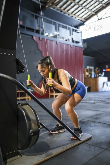 Vertical photo of a Chinese strong woman bending while pulling weights with a lat machine in a cross training gym