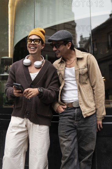A joyful gay couple shares a moment of laughter while looking at a smartphone. They stand together outside, dressed casually, radiating happiness and companionship